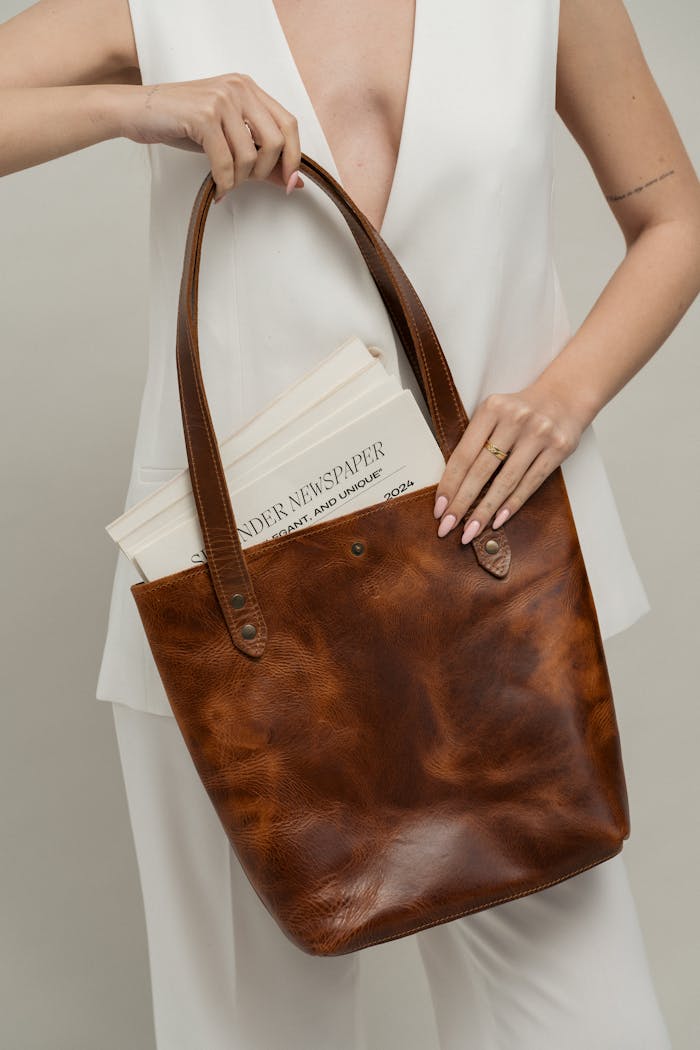 Mastering the First Impression: Your intriguing post title goes here Close-up of a fashionably dressed woman holding a leather tote bag with a newspaper.