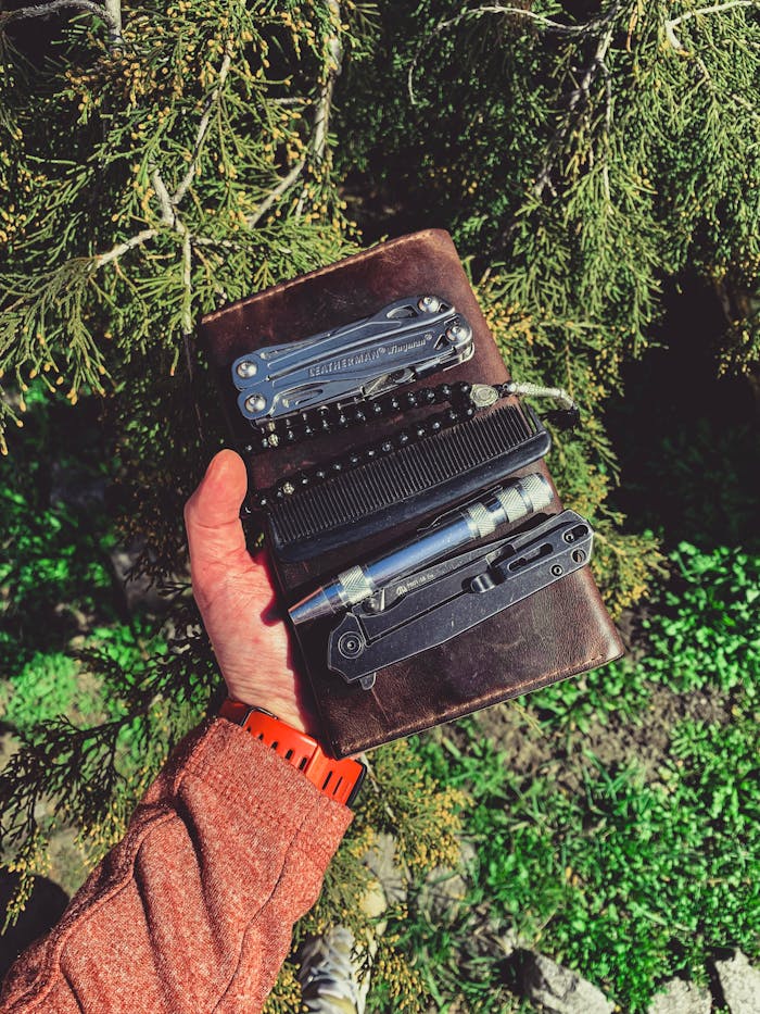 The Art of Drawing Readers In: Your attractive post title goes here A person holding a leather case with multitools amidst lush green foliage, showcasing adventure readiness.