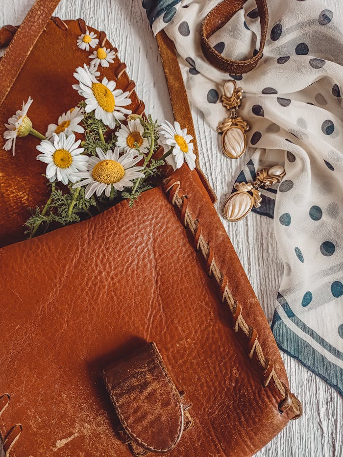 Crafting Captivating Headlines: Your awesome post title goes here Charming arrangement of a leather bag with daisies and jewelry on a wooden surface.